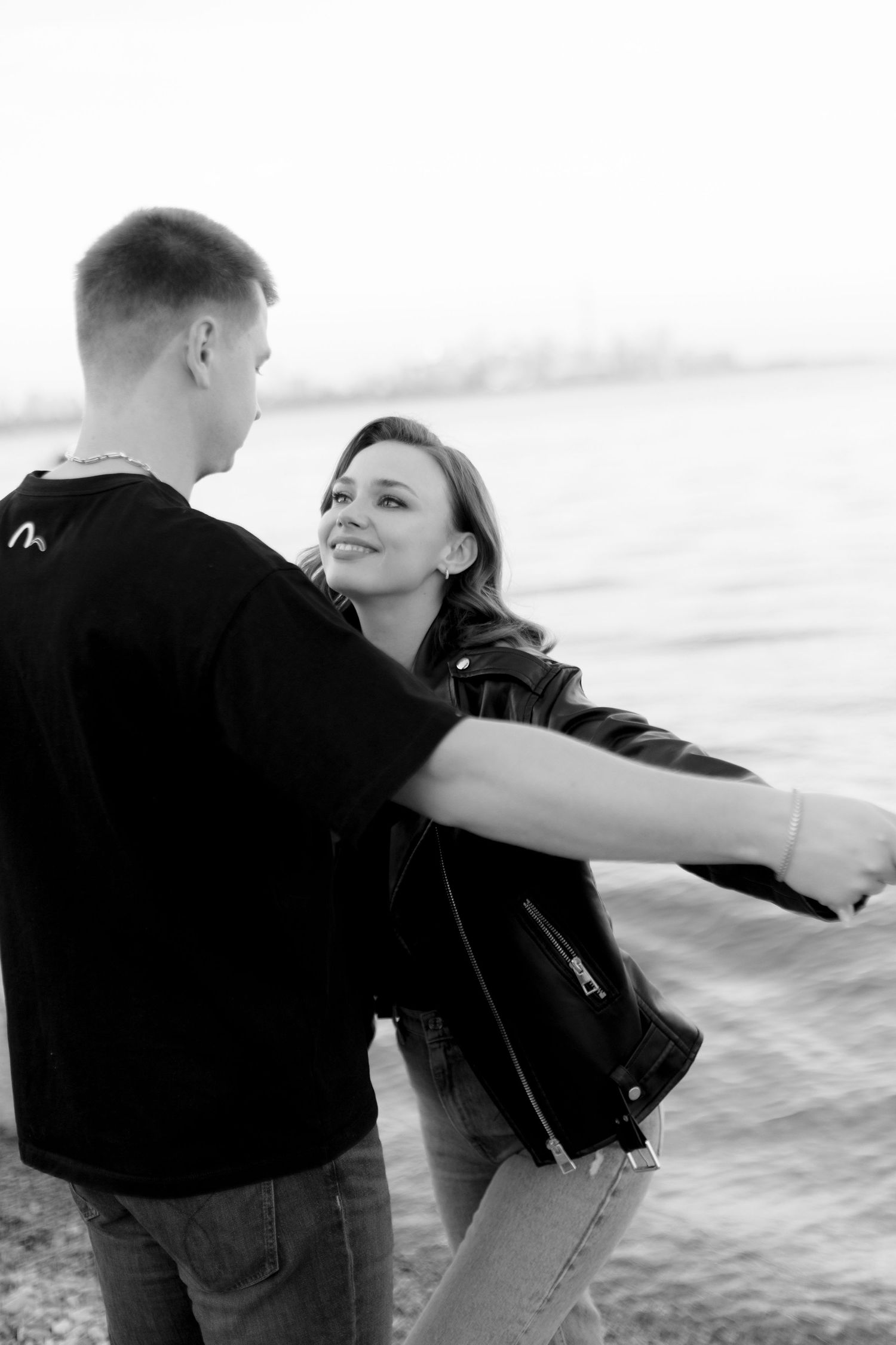 Black and white photo of couple sharing joyful moment by waterfront.