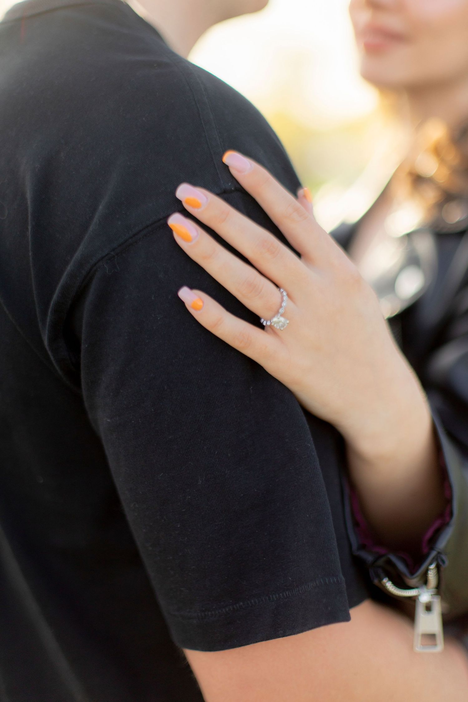 A close-up of a hand wearing an engagement ring resting on a black shirt sleeve.