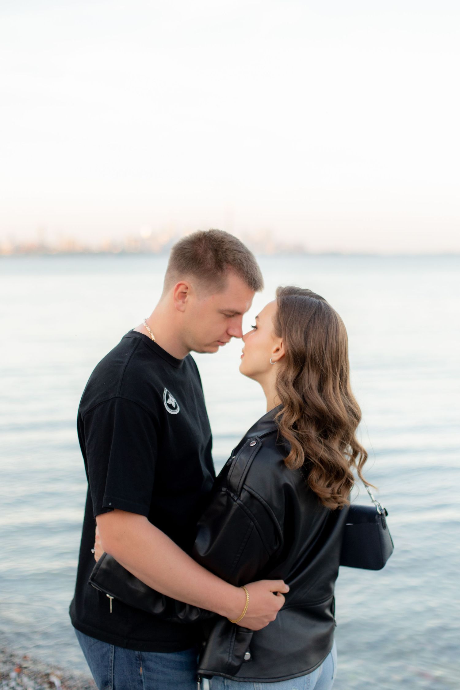 A romantic moment between two people in matching black outfits by the waterfront at dusk.