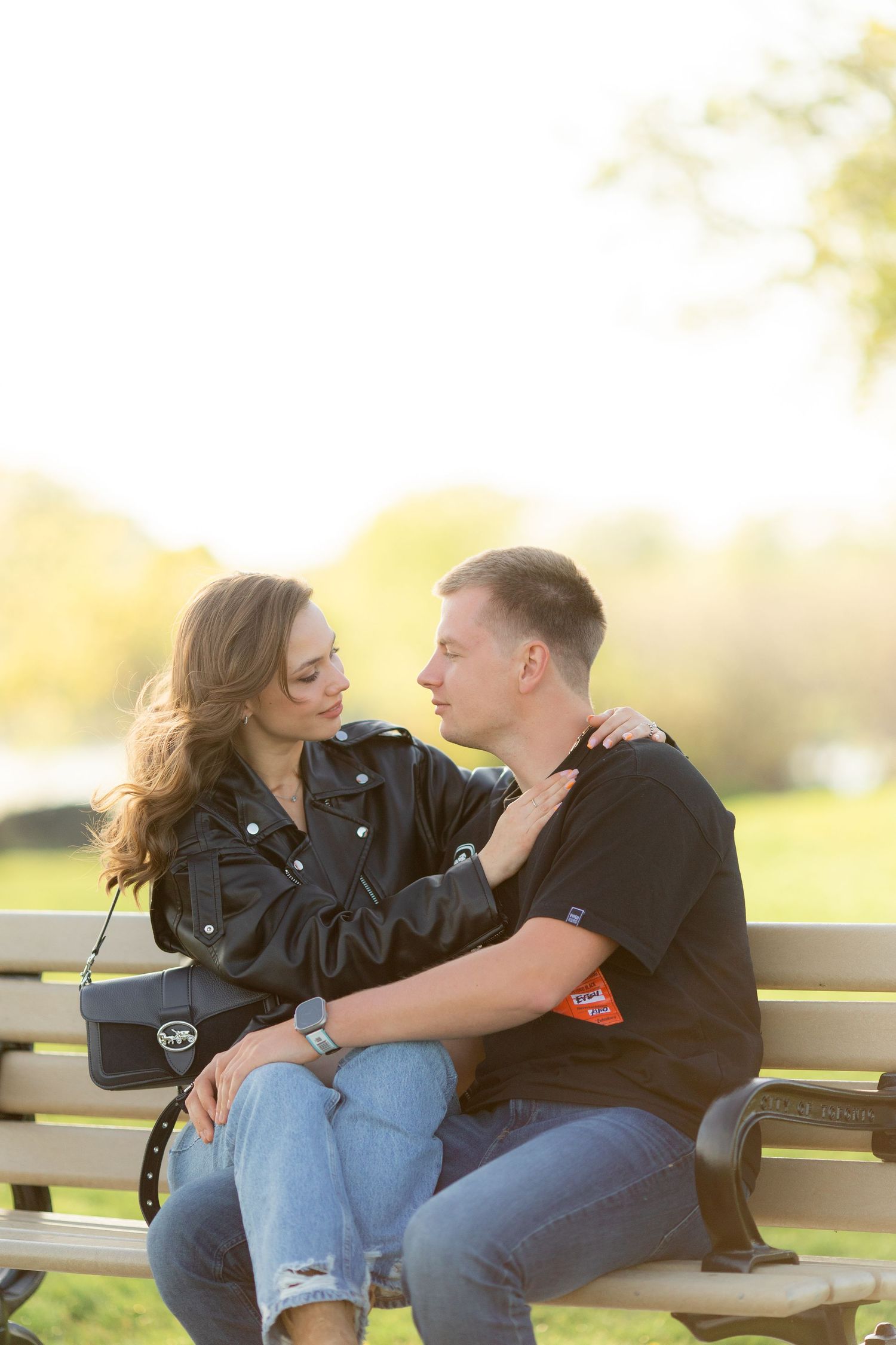 A romantic couple sitting close together on a park bench at sunset.