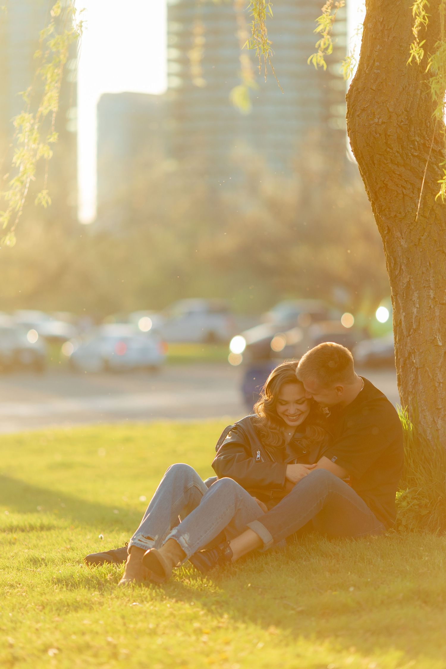 A tender moment shared under a tree during golden hour with parked cars in the background.