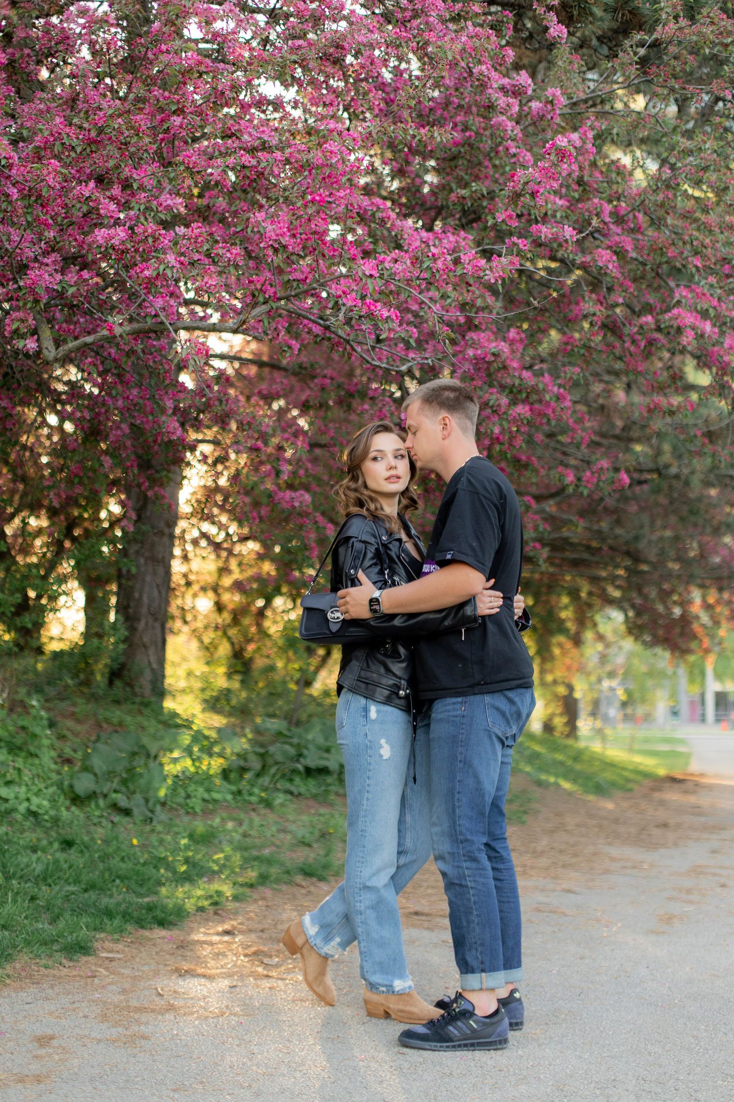 A couple embraces under blooming pink cherry blossoms on a spring evening path.