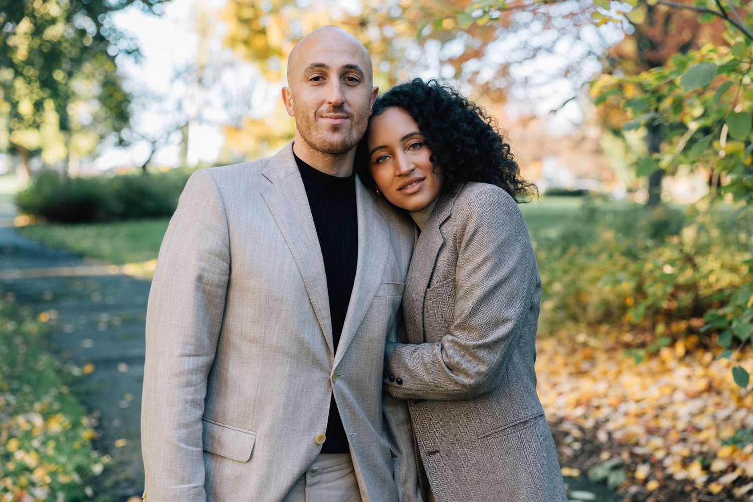 Stylish interracial couple posing together in autumn park with fall leaves.