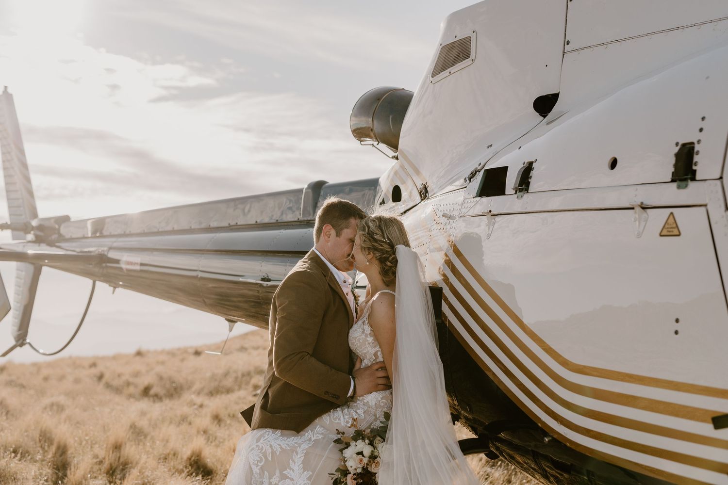 Couple shares romantic moment next to small aircraft during sunset photo session.