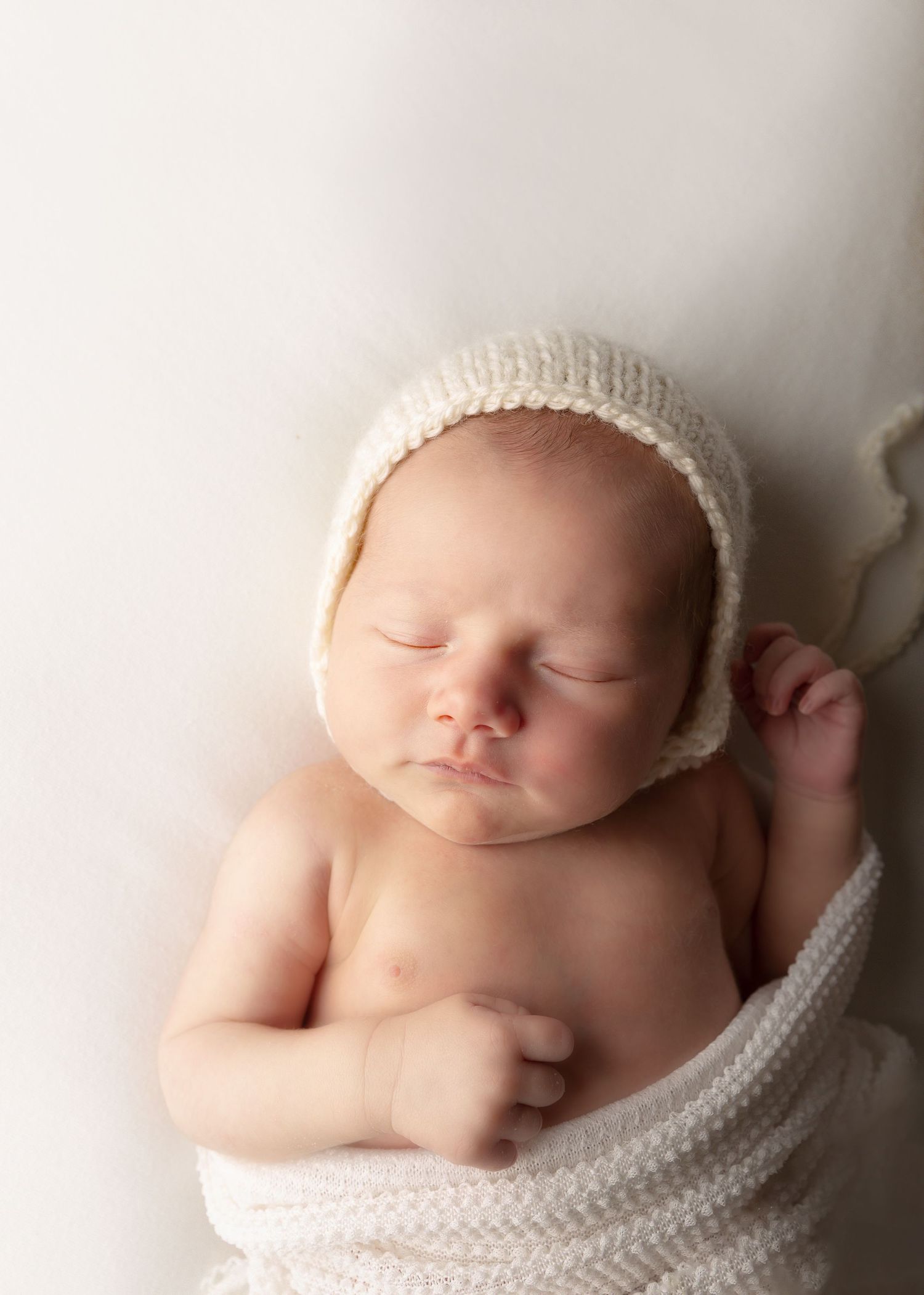 peaceful sleeping newborn wrapped in cream blankets and bonnet.