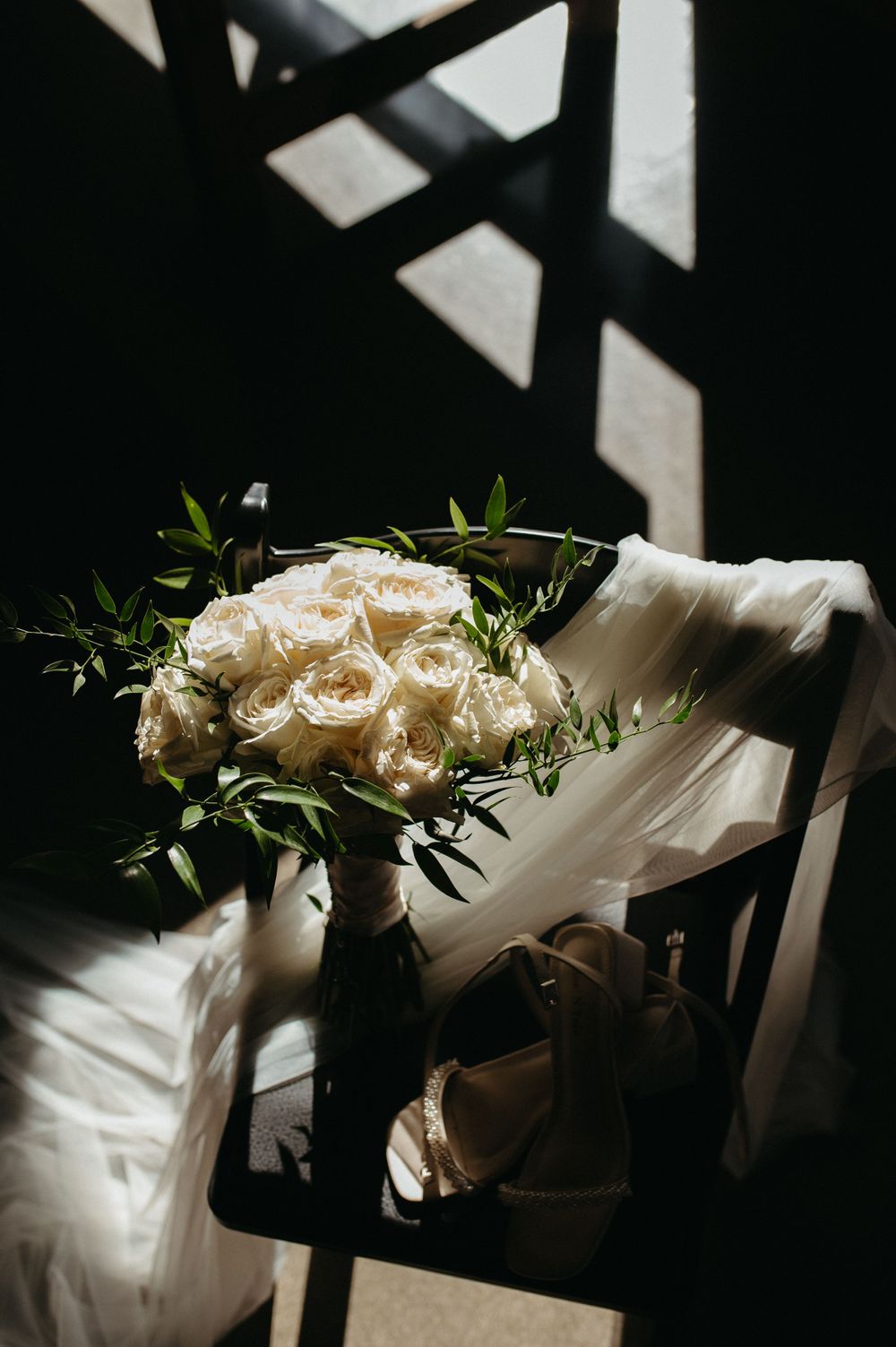 White rose bouquet and wedding dress fabric in dramatic window lighting.