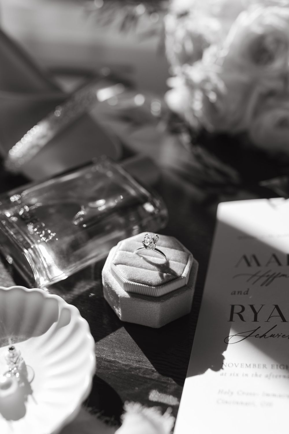 Black and white detail shot of wedding ring box and invitation on wooden surface.