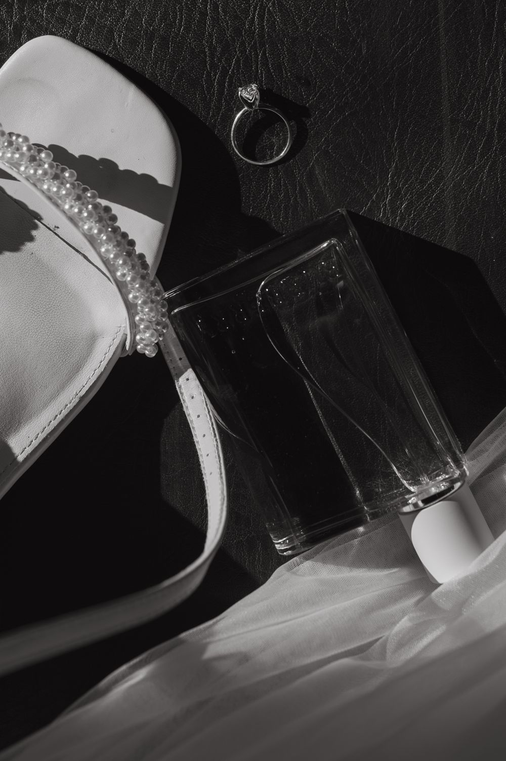 Close-up of sparkly bridal shoe with diamond ring and champagne glass in black and white.