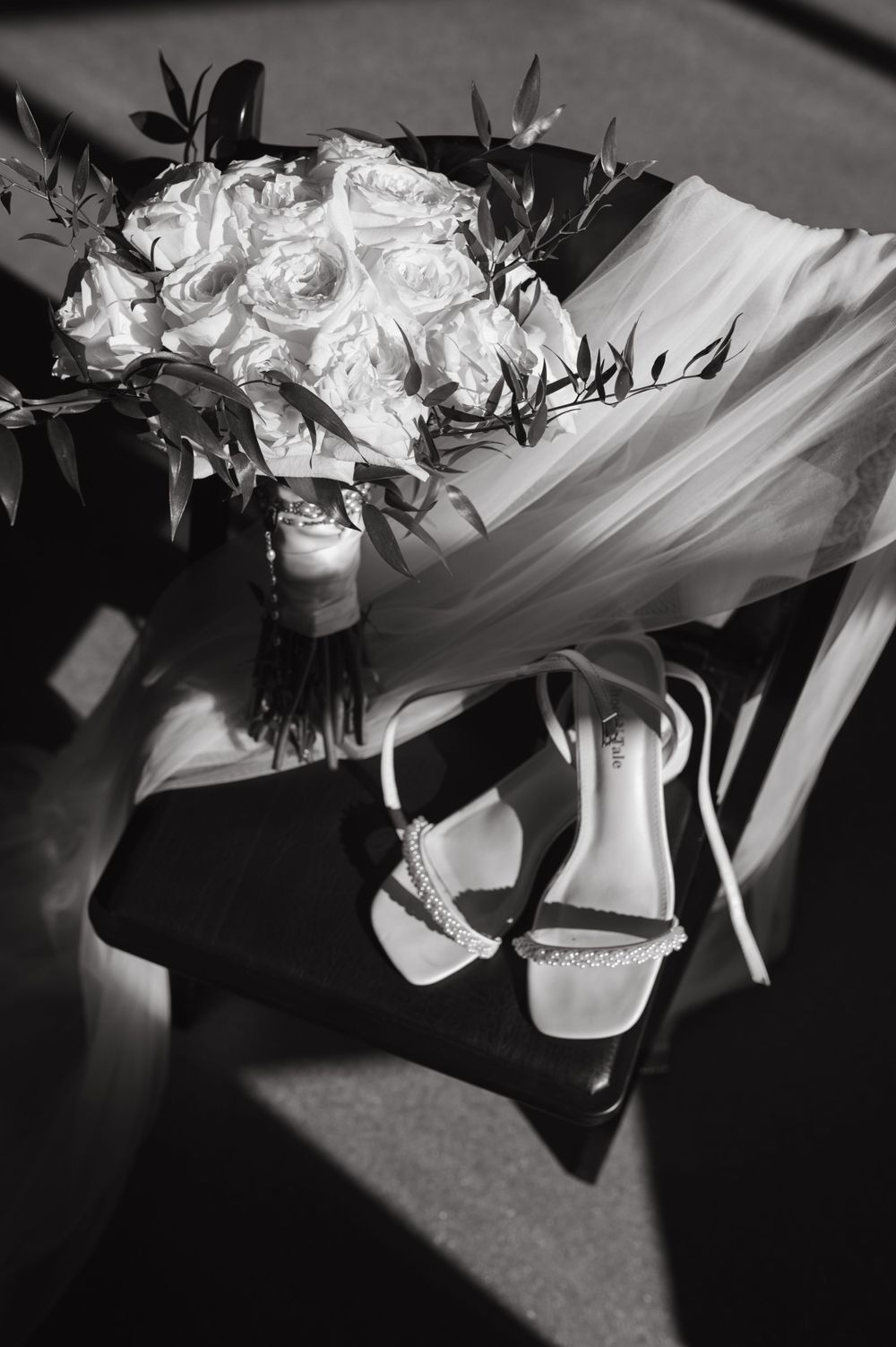 Black and white image of bridal bouquet with white roses and wedding shoes.