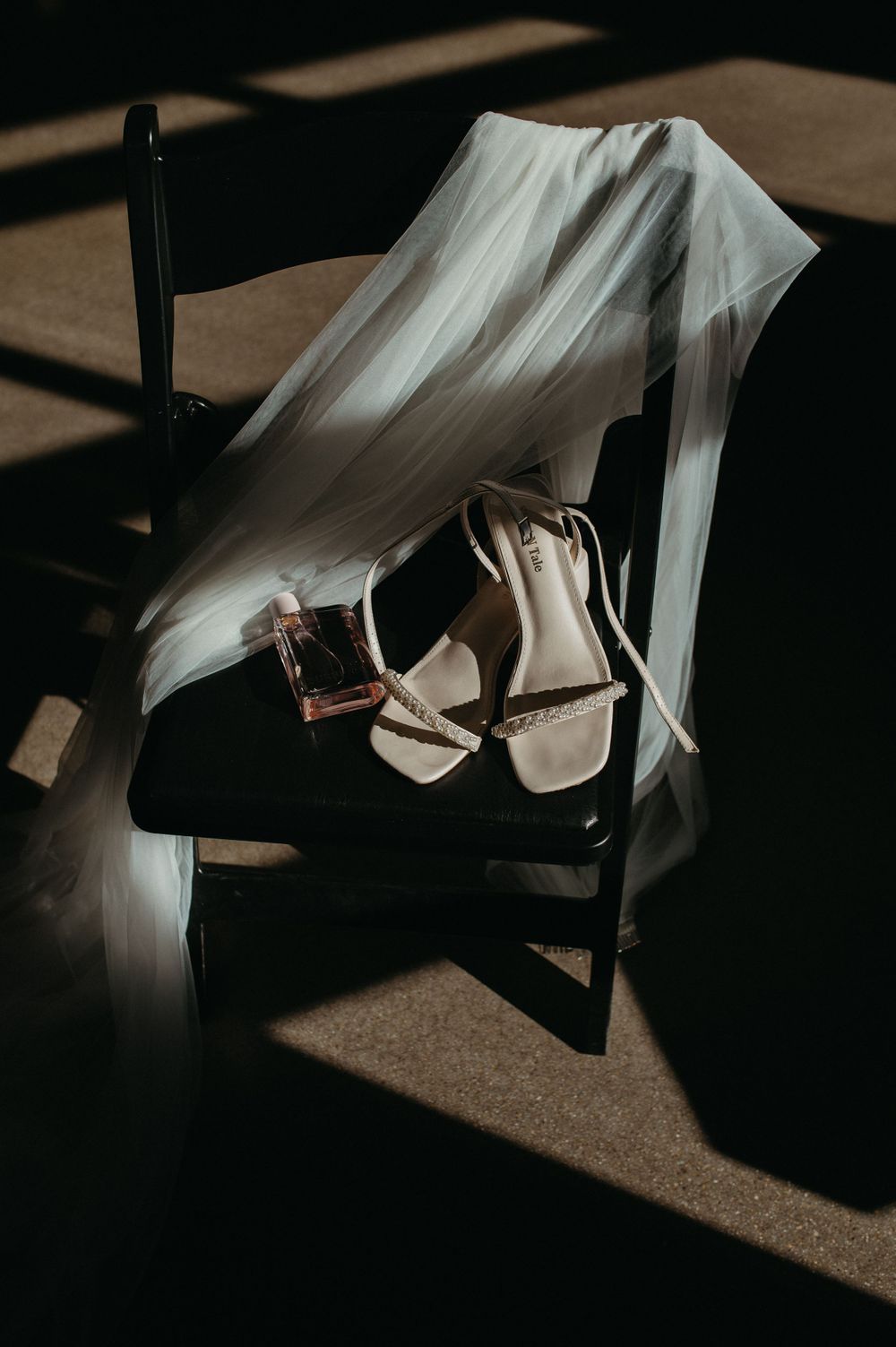 Wedding veil draped over chair with elegant sandals in moody lighting.