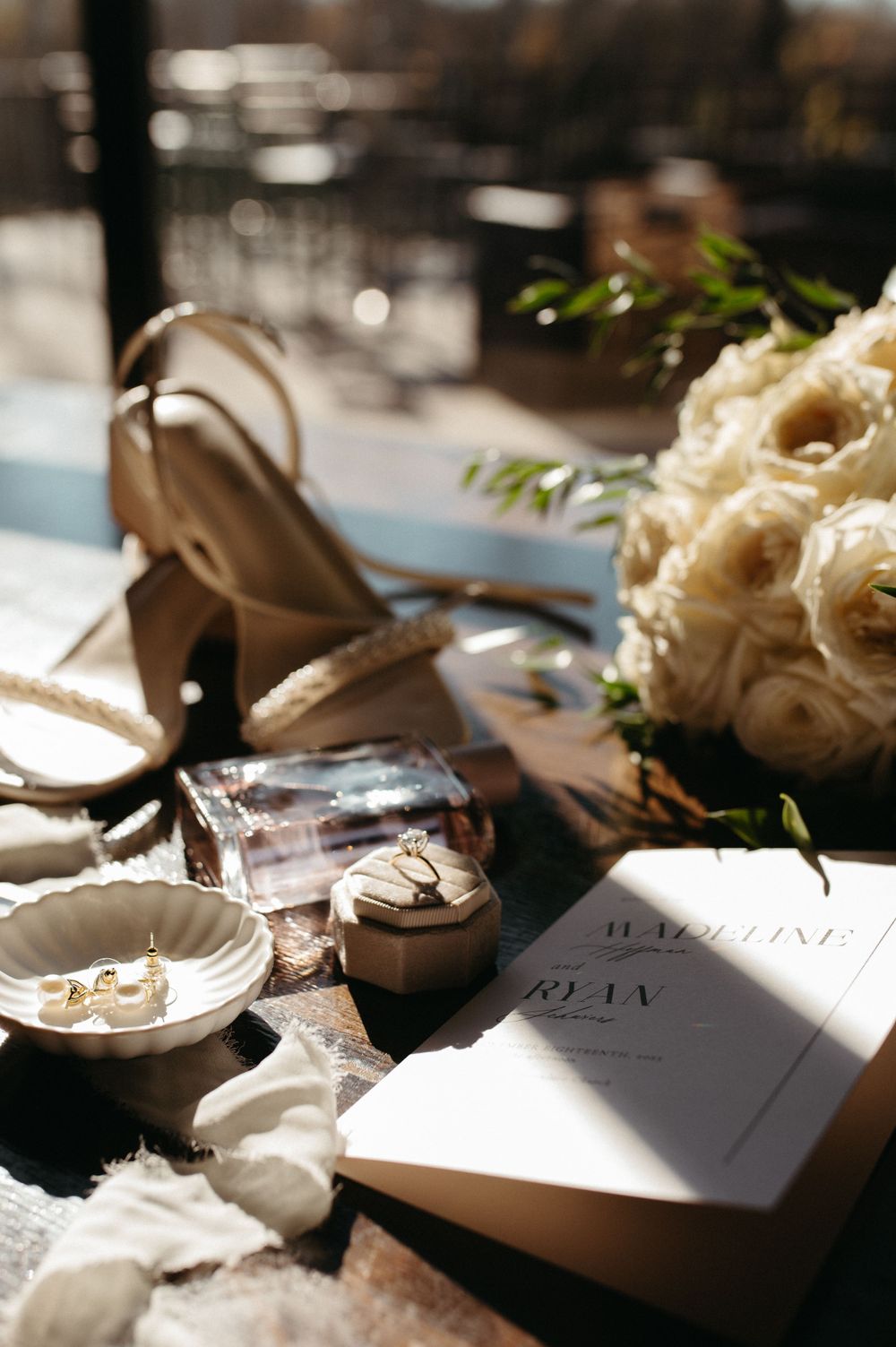 Elegant wedding accessories including bridal shoes, bouquet, and invitation laid out on wooden surface.