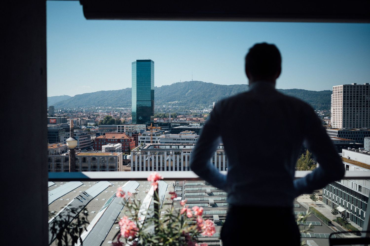 Silhouette of someone looking at city skyline with tall building against mountains.