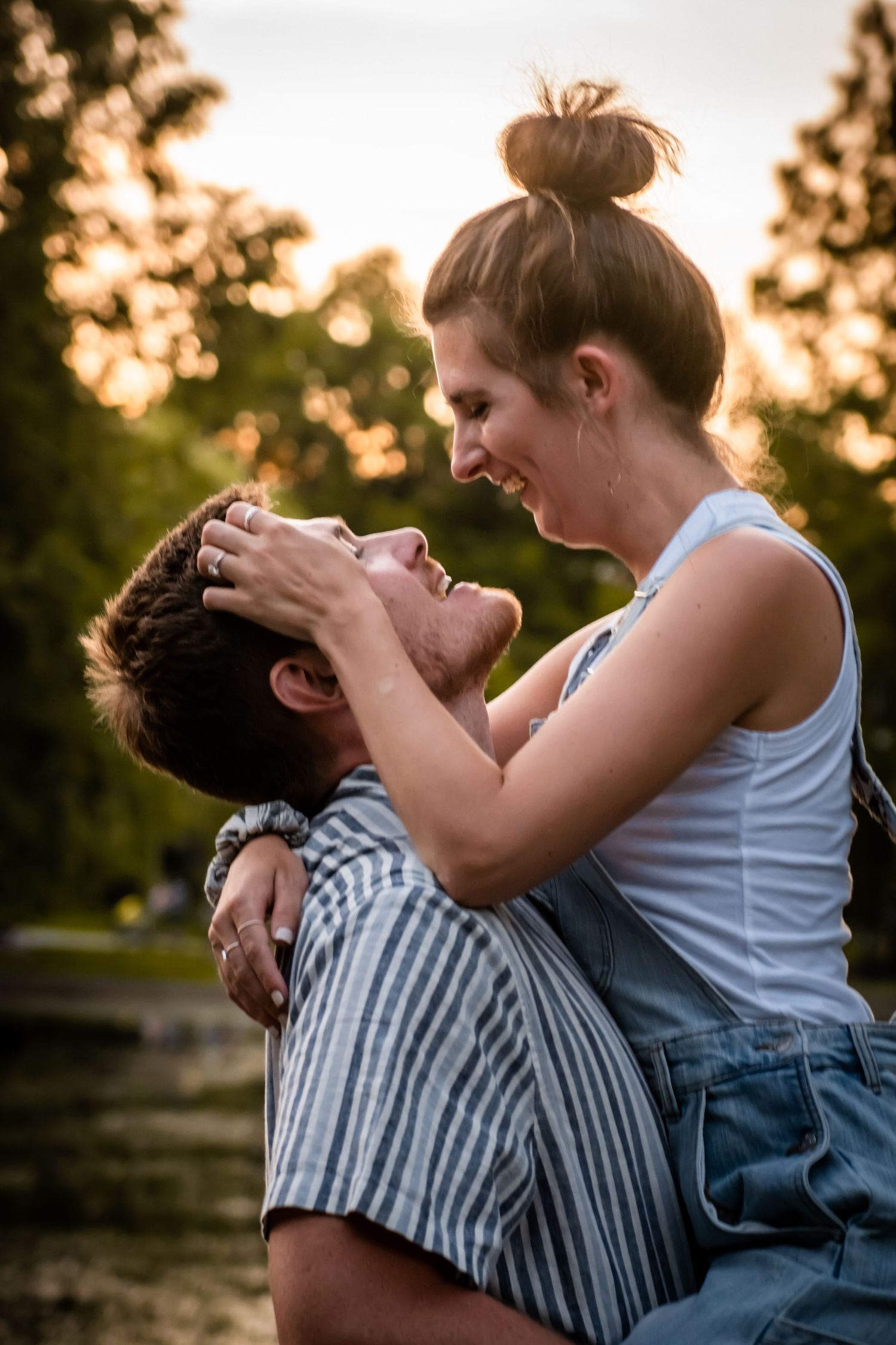 A playful couple shares a joyful moment at sunset in a park setting.