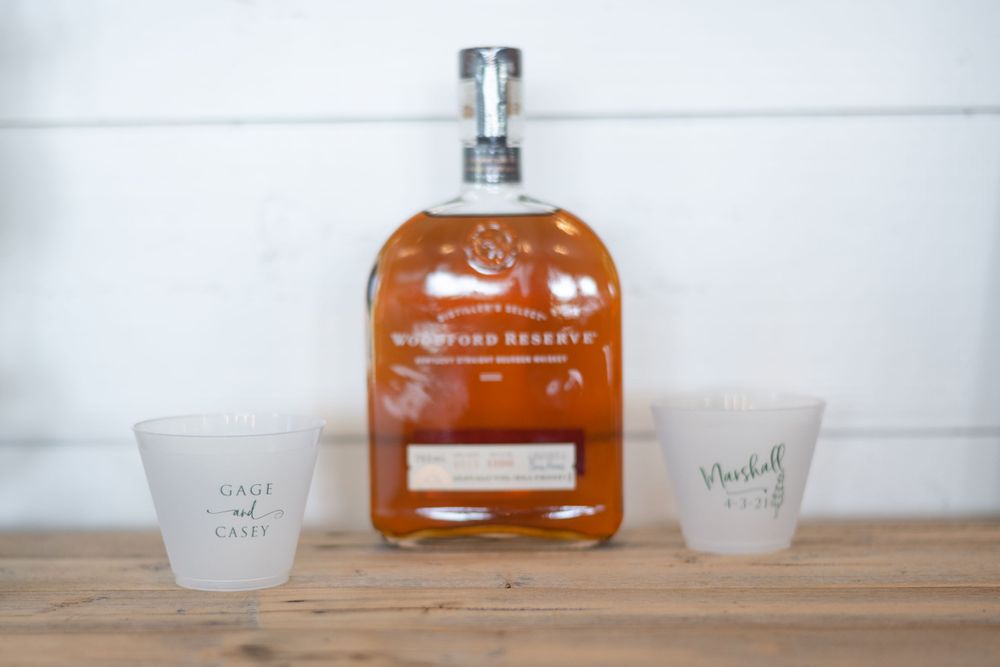 Glass bottle of bourbon with two frosted shot glasses on wooden surface.