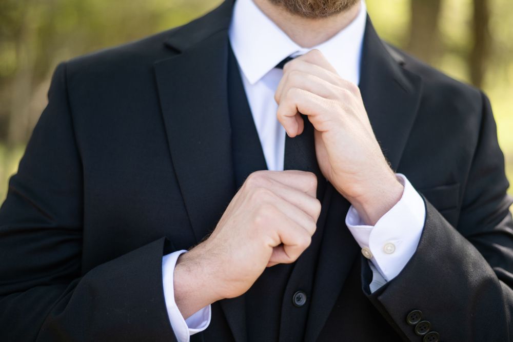 Close-up detail of hands adjusting tie and suit jacket.