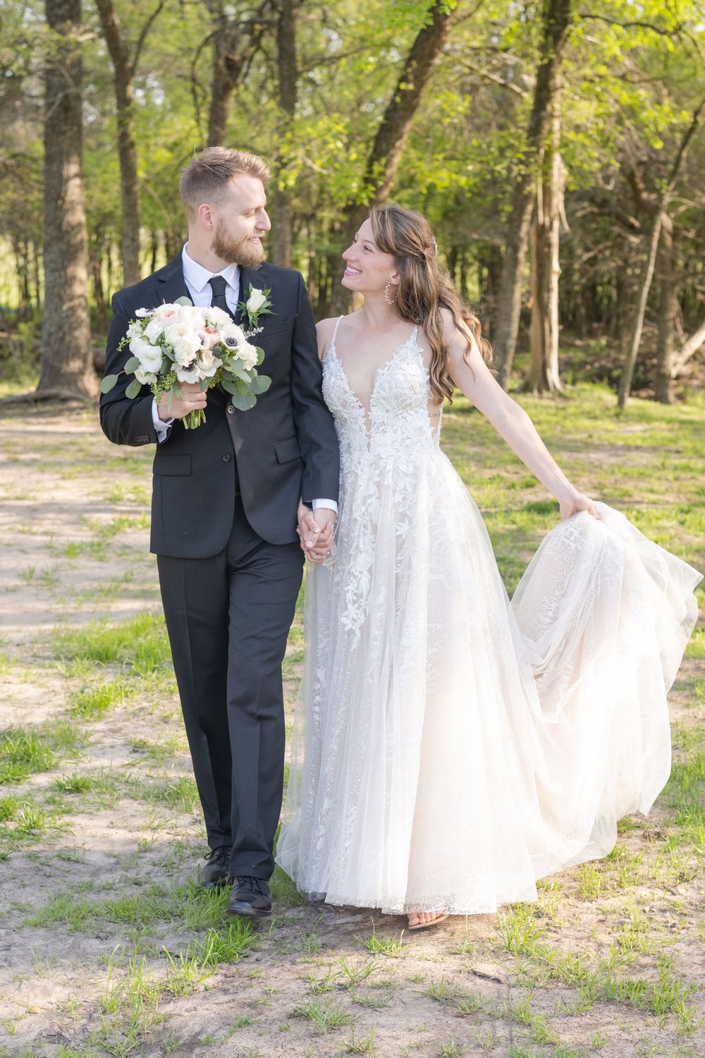 A romantic wedding couple walking together outdoors with the bride in a lace gown holding her dress.