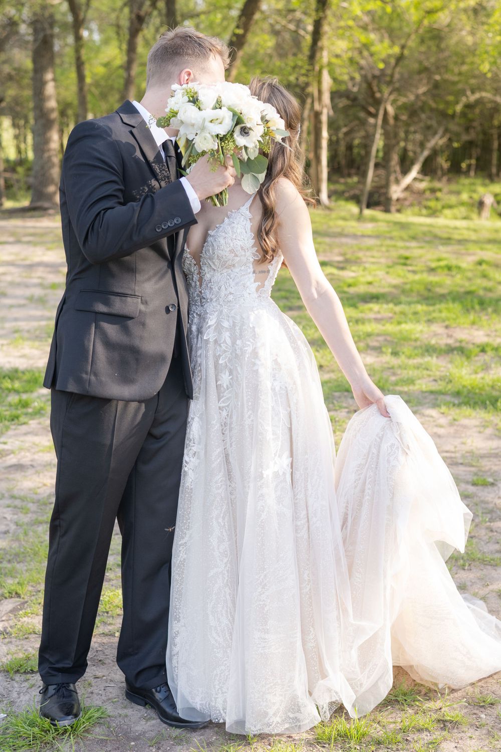A couple shares a tender moment with white flowers in a wooded outdoor setting.