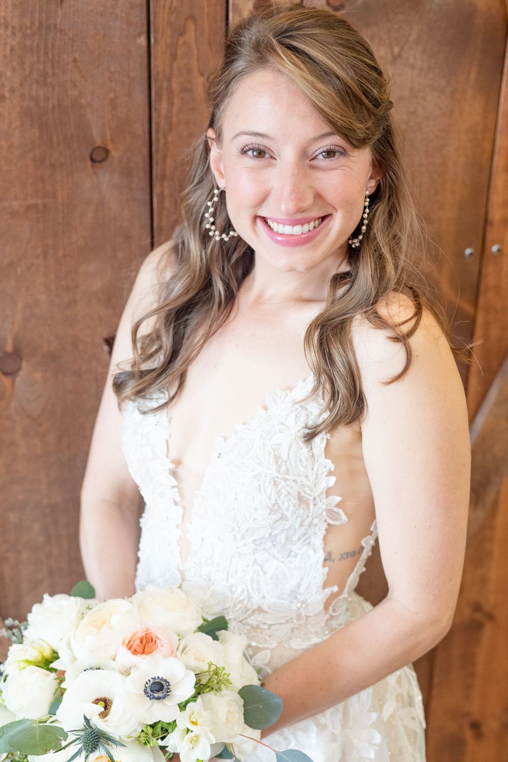 A bride in a lace wedding dress holds a white and peach bouquet against wooden backdrop.