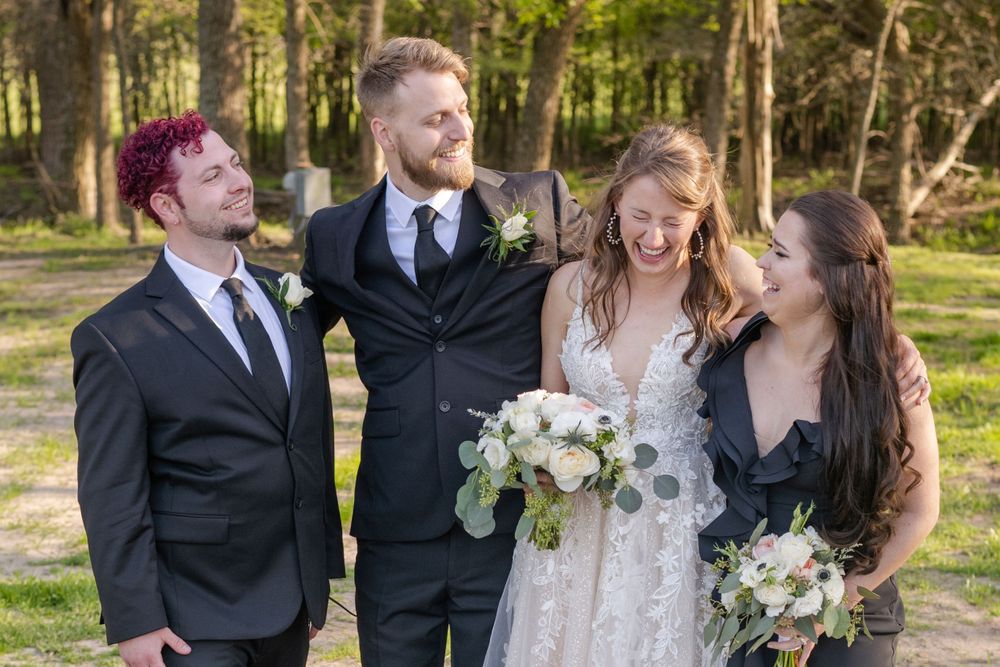 Wedding party of four people sharing laughter together in an outdoor forest setting.
