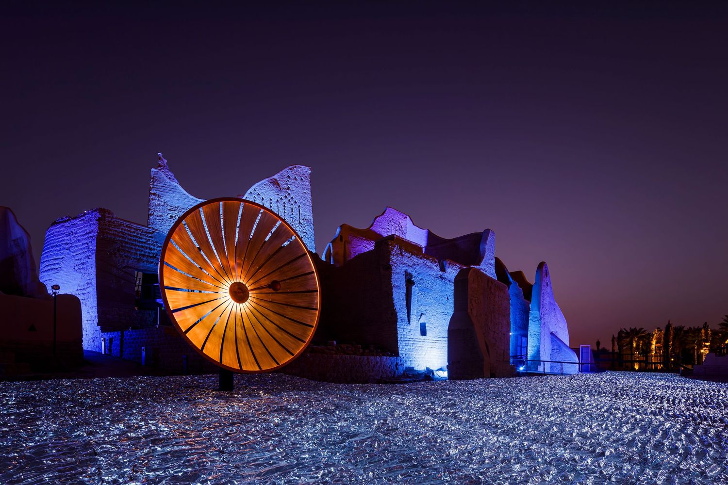 Illuminated circular art installation glows orange against blue-lit ruins at night.