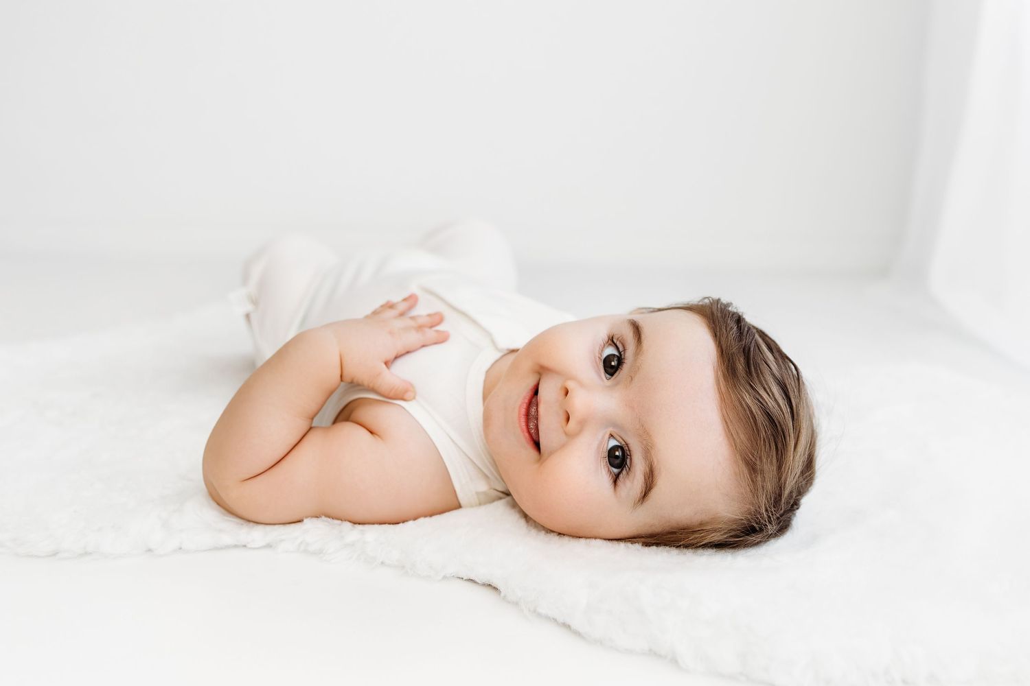 Grinning baby laying sideways on white fur rug