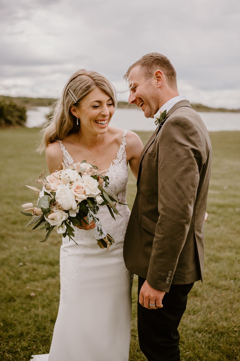 Candid wedding moment with couple laughing together holding elegant floral bouquet.