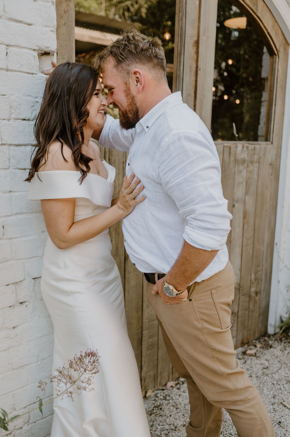 Wedding couple sharing an intimate moment against white brick wall and rustic door.