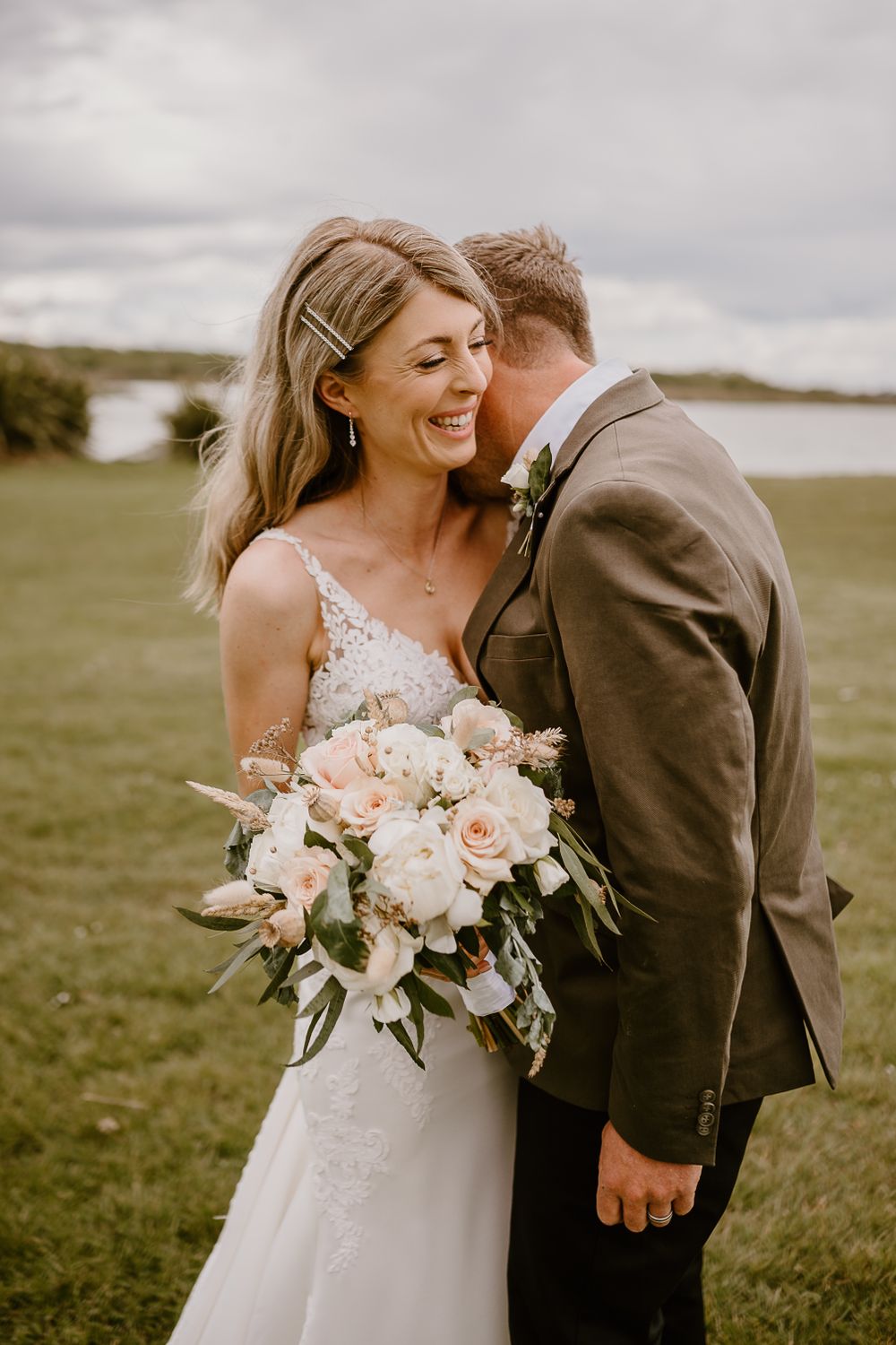 Joyful wedding moment captured outdoors with elegant bouquet and cloudy sky backdrop.