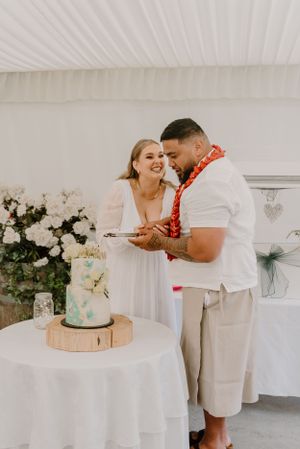 Couple sharing cake at their wedding reception with white floral decorations and a blue-accented cake.