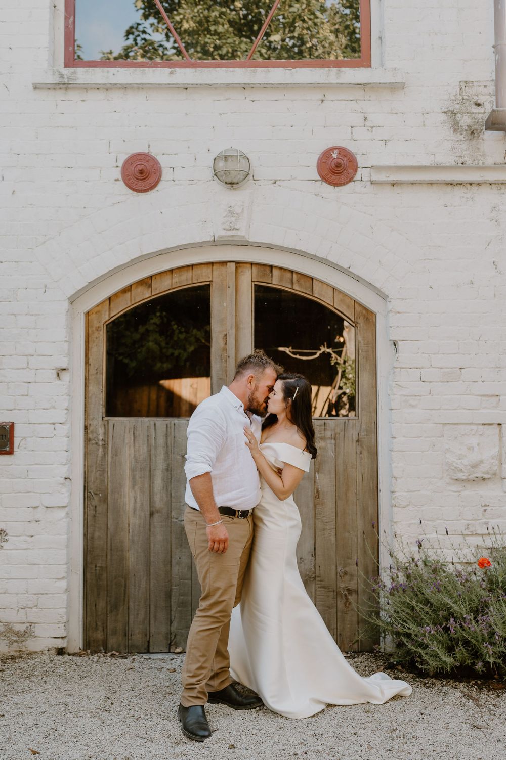 An intimate moment between newlyweds against a weathered white brick wall and wooden door.