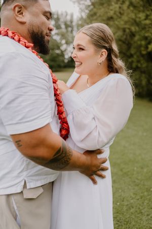 Wedding couple embracing and laughing outdoors with red lei detail.