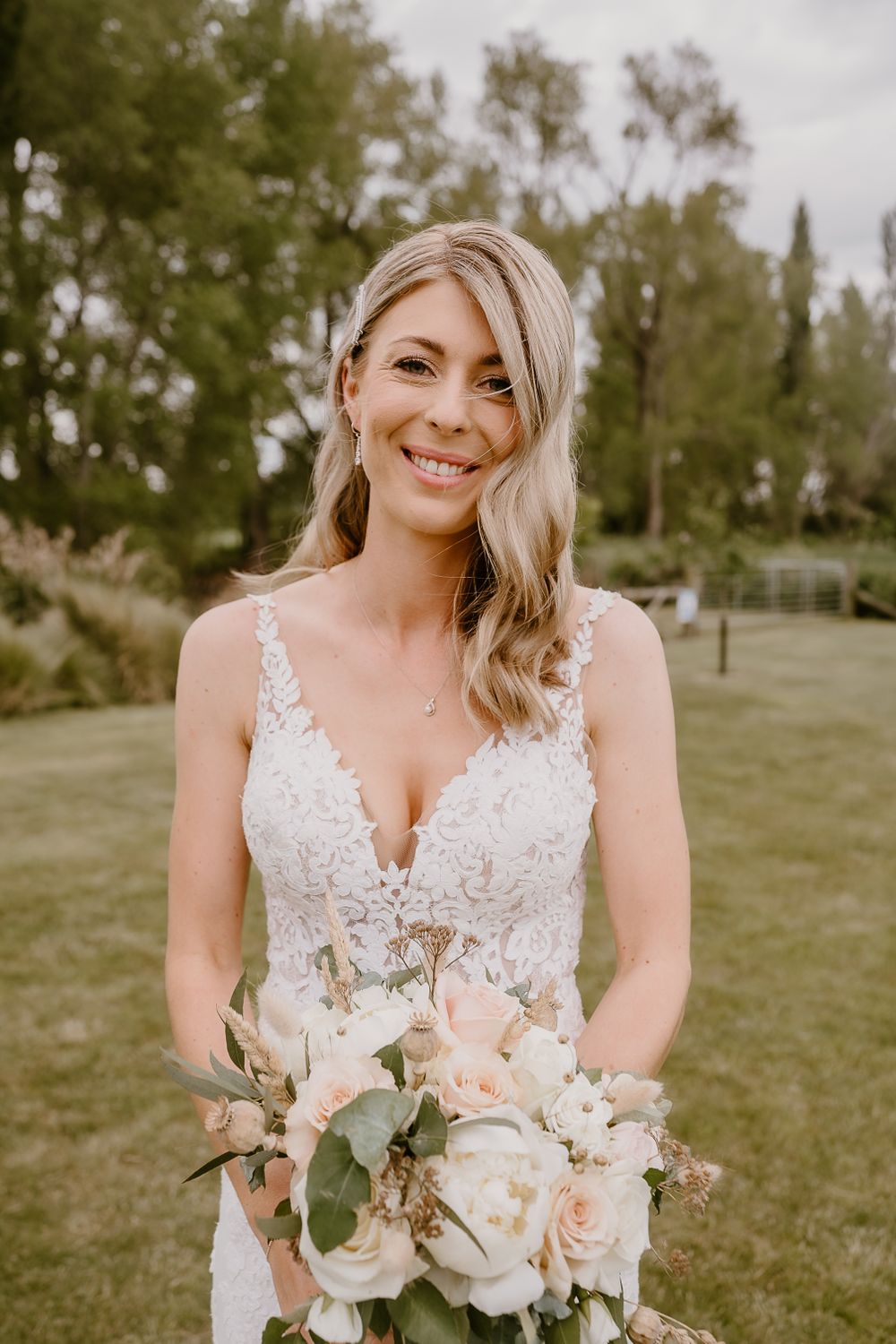 Bride holding a soft pink and white rose bouquet in an outdoor garden setting.