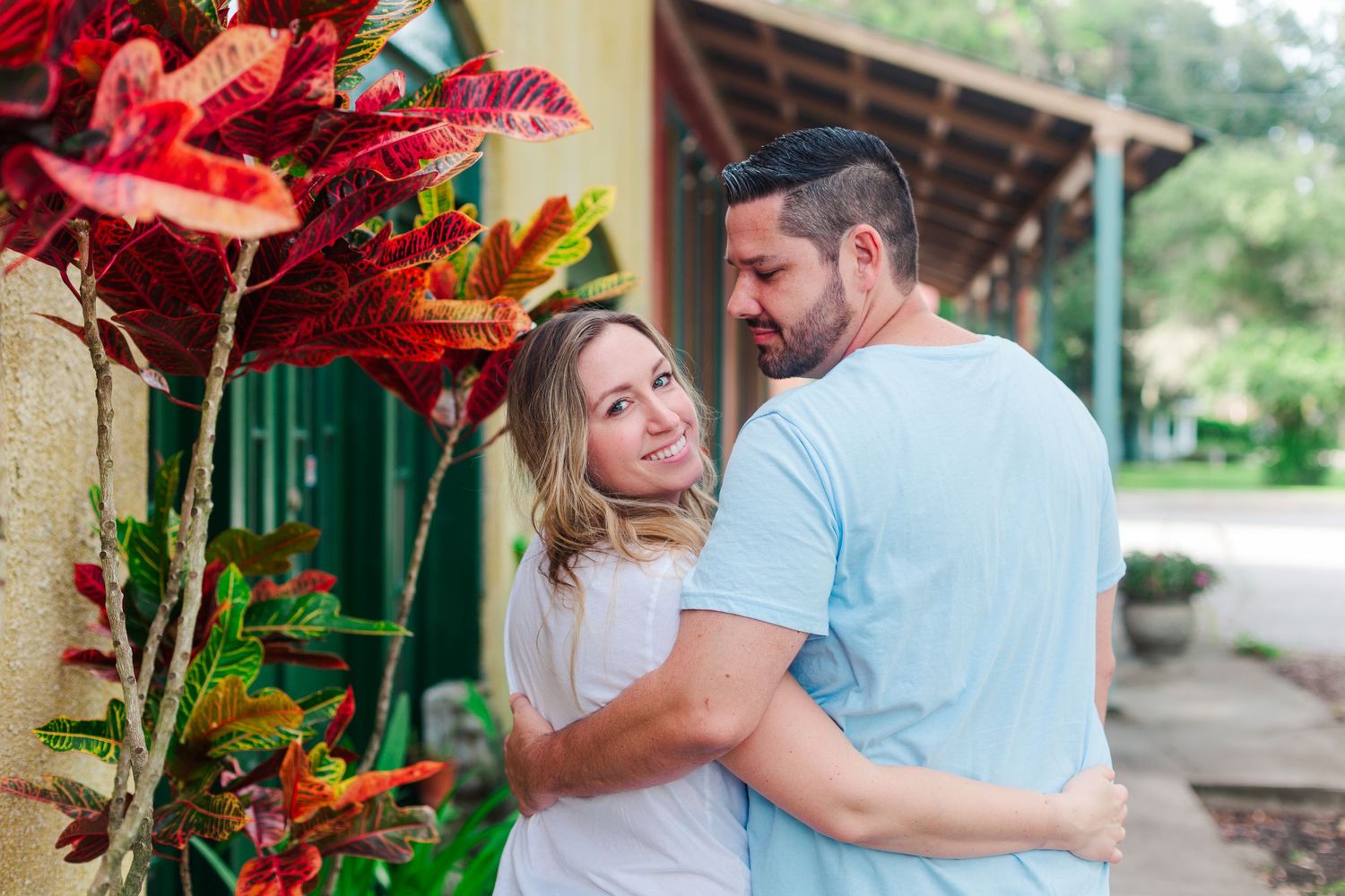 Couple embracing in front of vibrant tropical red flowers and greenery.
