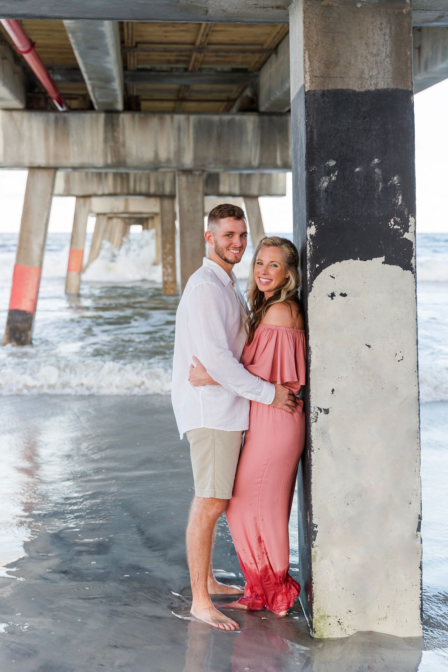 Playful beach pier photoshoot with concrete pillars and coastal backdrop.