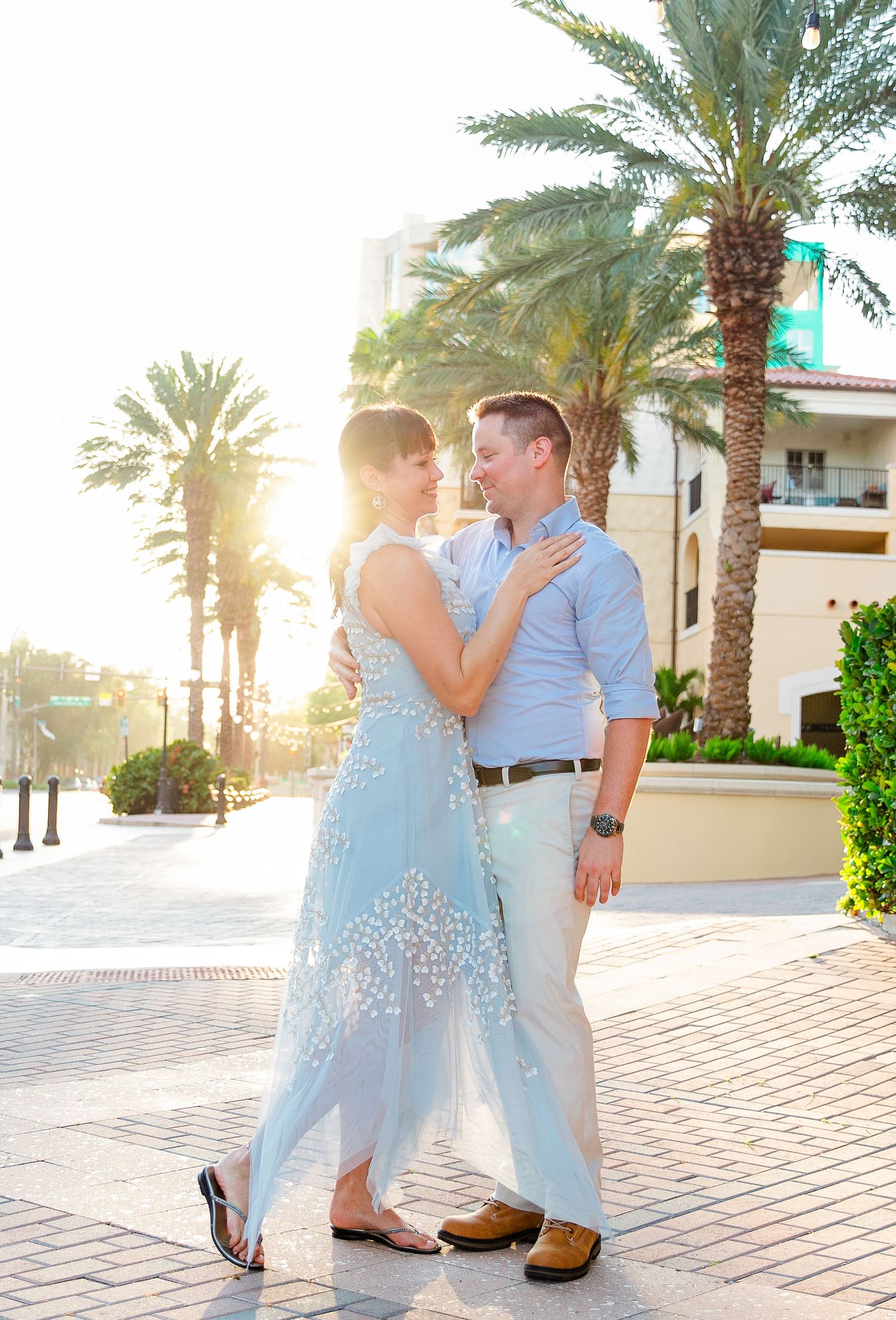 Romantic couple poses on brick pathway with palm trees and golden sunlight.