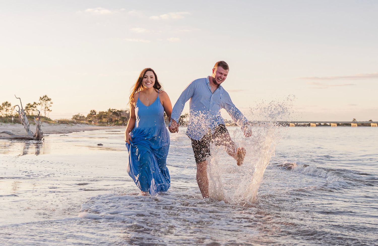 Couple splashing and playing in ocean waves at sunset during beach photoshoot.