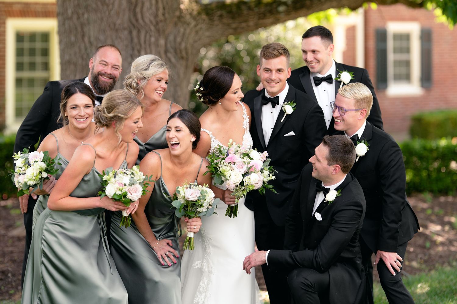 Wedding party laughs together outdoors in formal black tuxedos and white gowns.