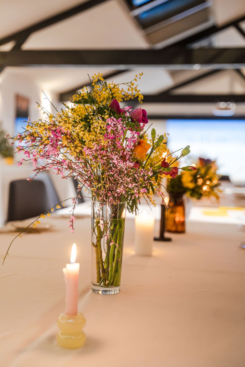 Row of elegant floral centerpieces with candles on a white tablecloth.
