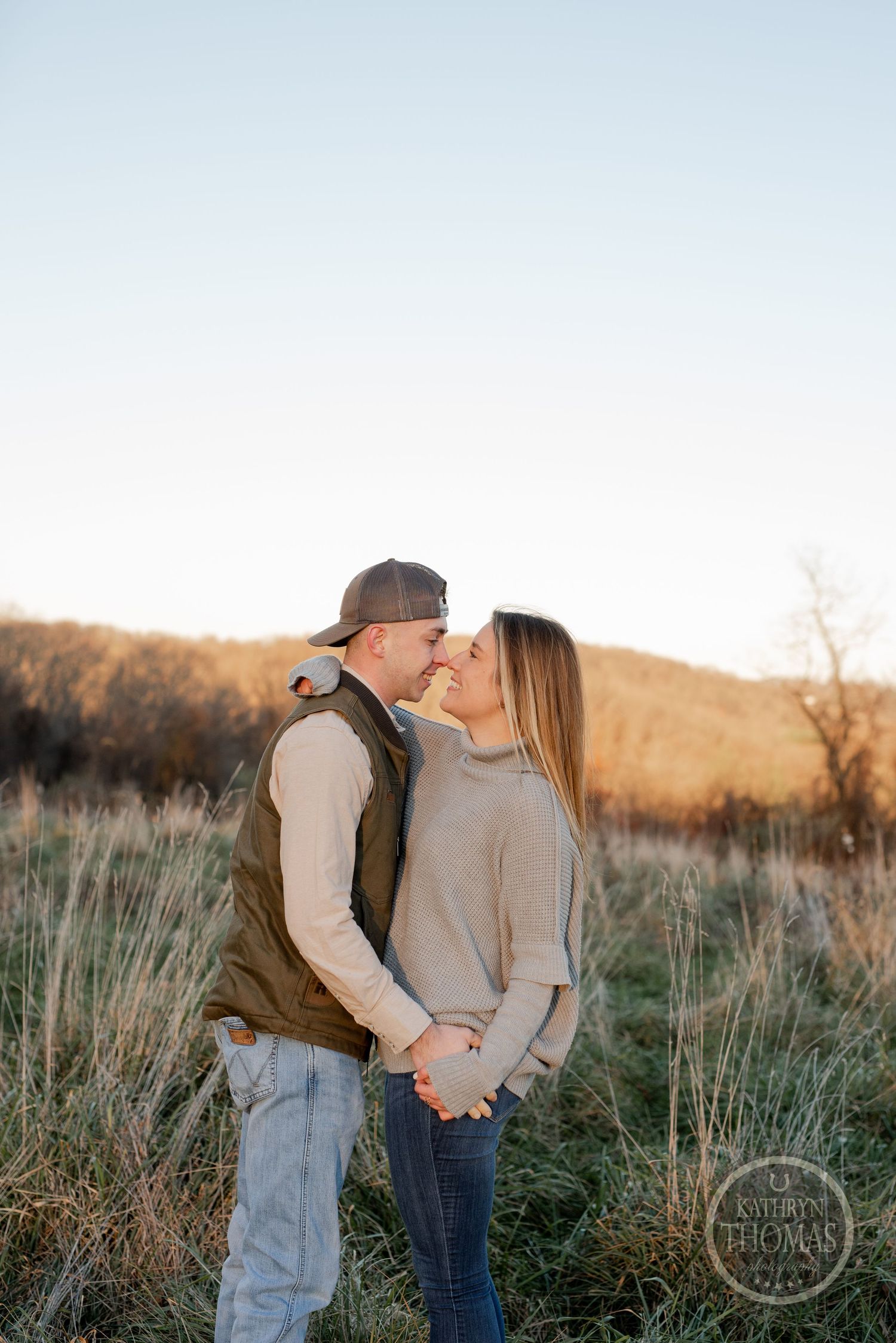 An intimate countryside portrait of a couple sharing a tender moment among autumn grasses at sunset.