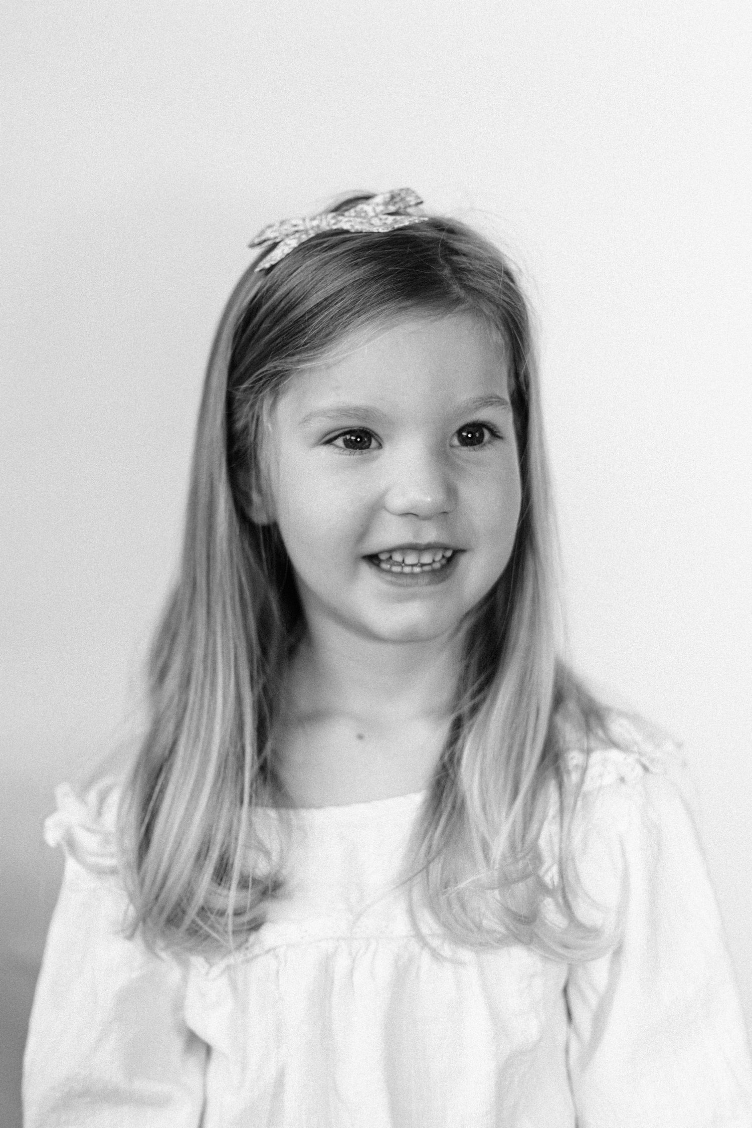 A black and white portrait showing a child in a white dress with shoulder-length hair.