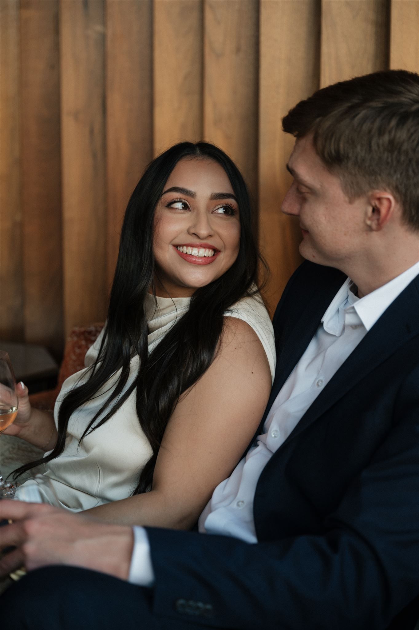 Happy couple relaxing on leather couch sharing drinks and smiles in cozy restaurant setting.