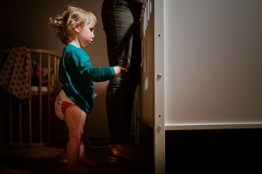 Young child exploring around dark furniture in a home setting.