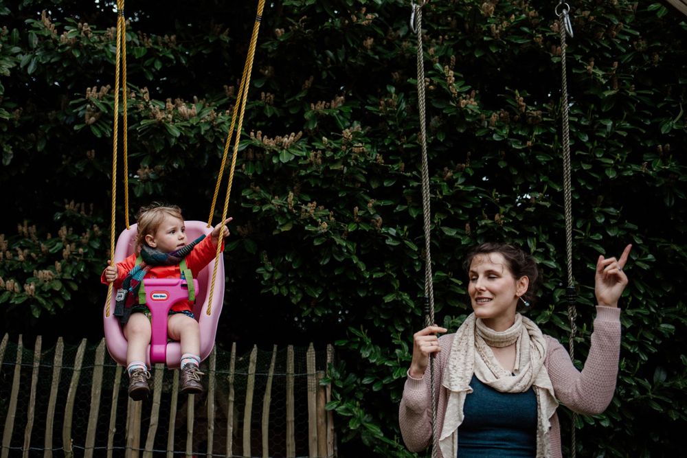A garden swing set photographed against lush green foliage on a sunny day.