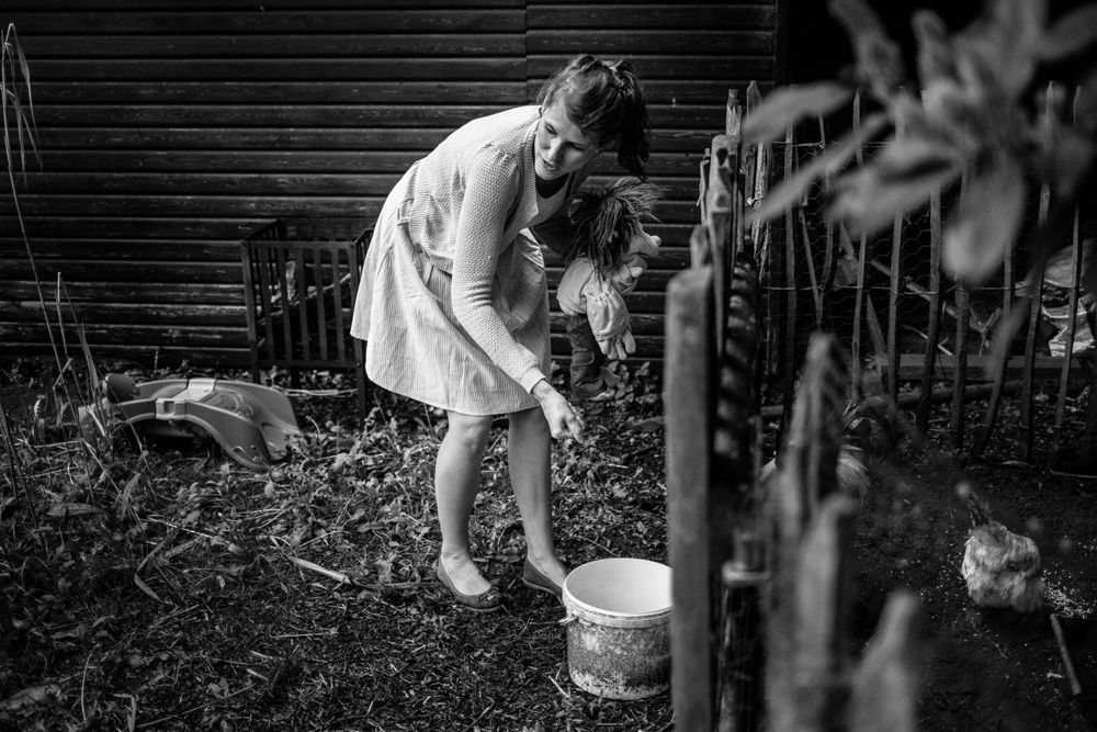 A black and white garden scene shows someone tending to plants with a bucket.