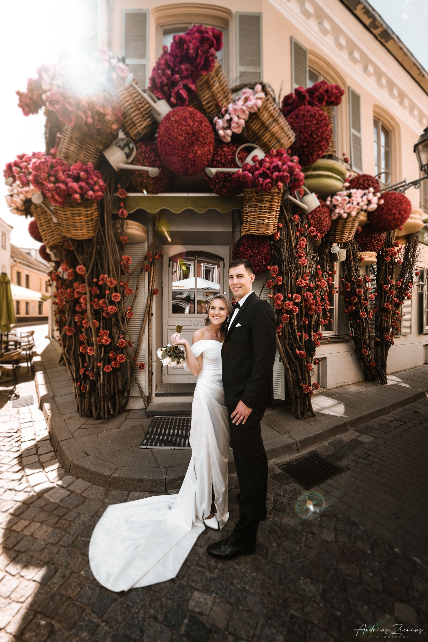 Elegant wedding couple posing beneath a stunning floral archway with red blossoms and wicker baskets.