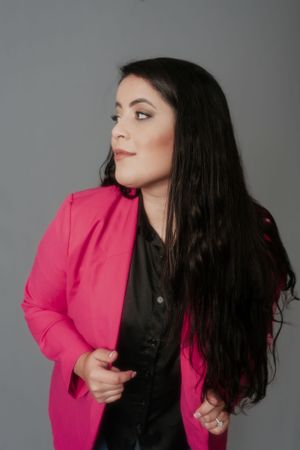 Stylish portrait featuring bright pink blazer and black shirt combination against gray background.
