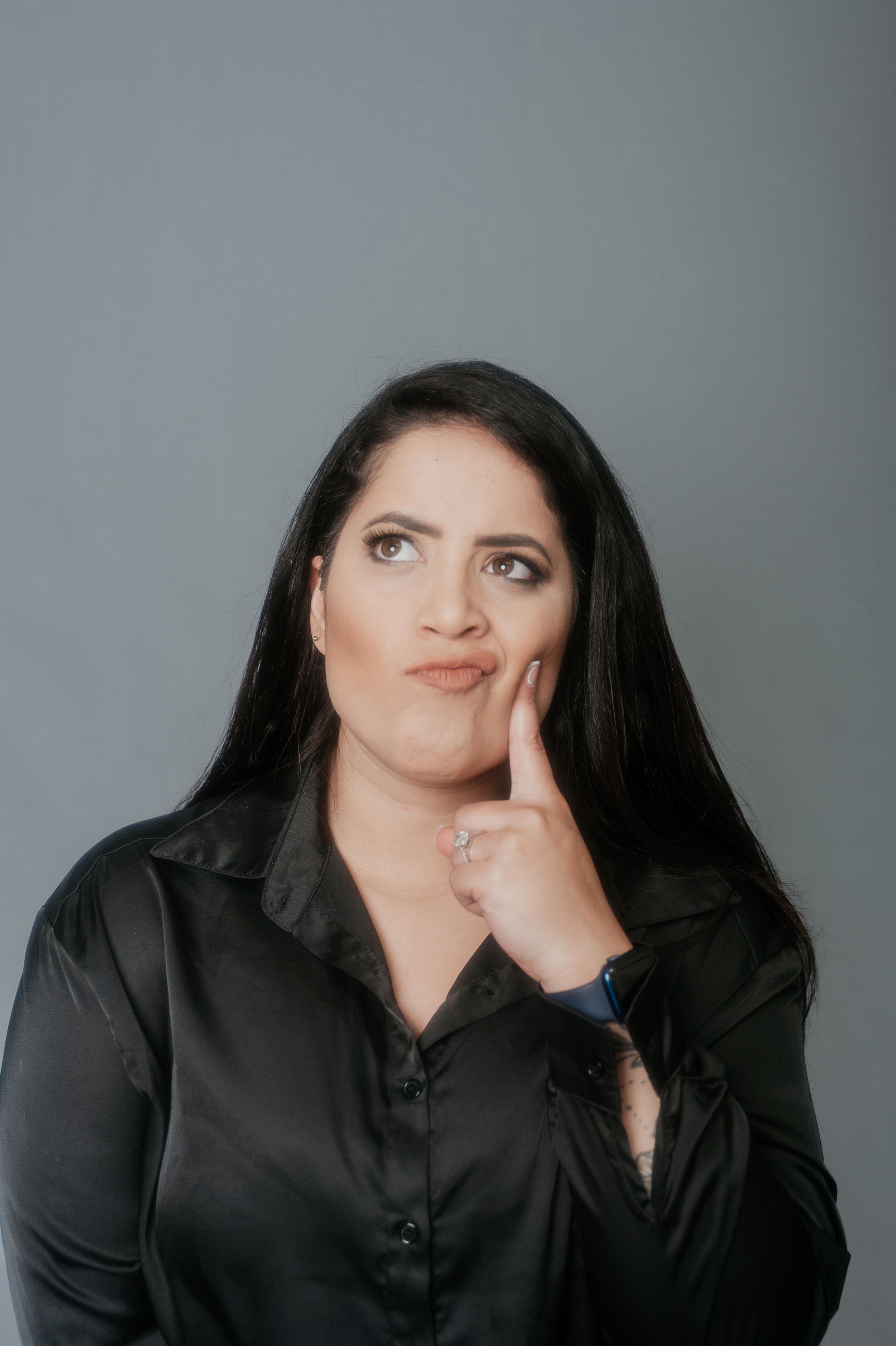 Studio portrait showing contemplative pose in black satin shirt against neutral backdrop.