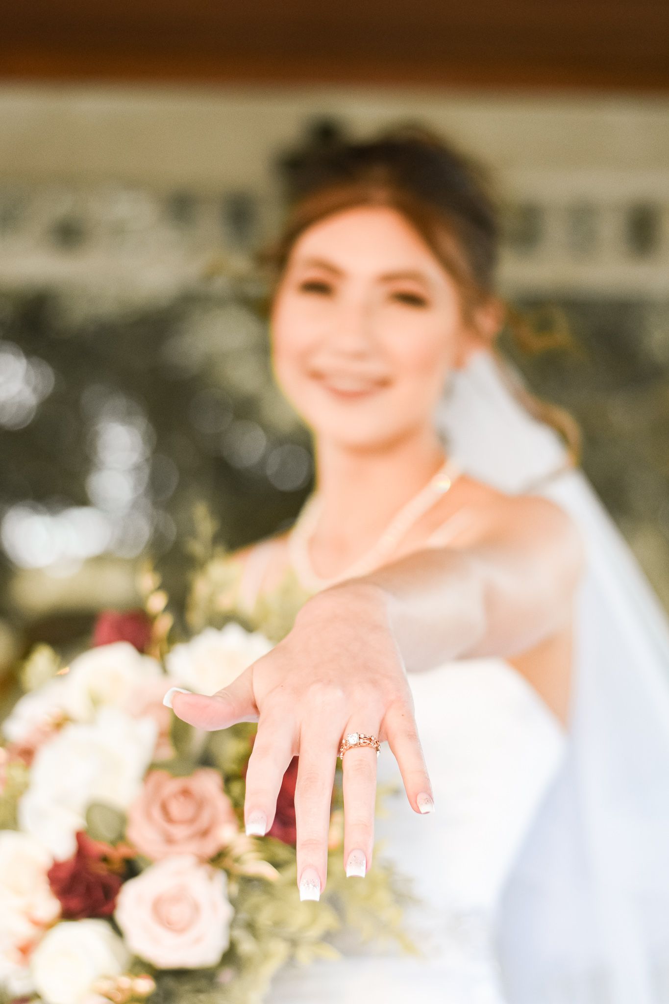 Close up of engagement ring with wedding bouquet in soft focus background.