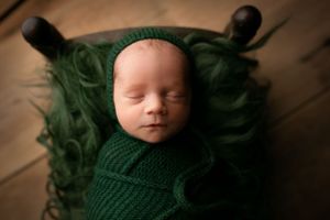 Newborn baby boy lying on a wooden bed. The fur and outfit he is wearing is hunter green. - Greenville SC newborn photographer - Easley SC