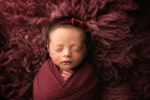 Newborn girl in a dark mauve wrap on the same color back. - Greenville SC newborn photographer - Easley SC newborn photographer